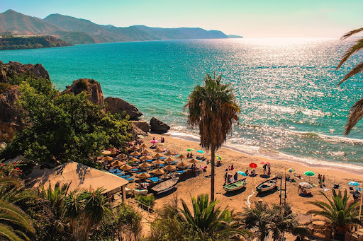 Nerja, Málaga. Sunny view of the Mediterranean Sea from Costa del Sol. With clean water, people at the sand and giant palm trees.