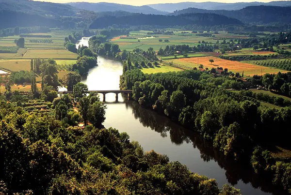 The river Dordogne winding through farmland and poplar trees beneath wooded hills, seen from the clifftop at Domme