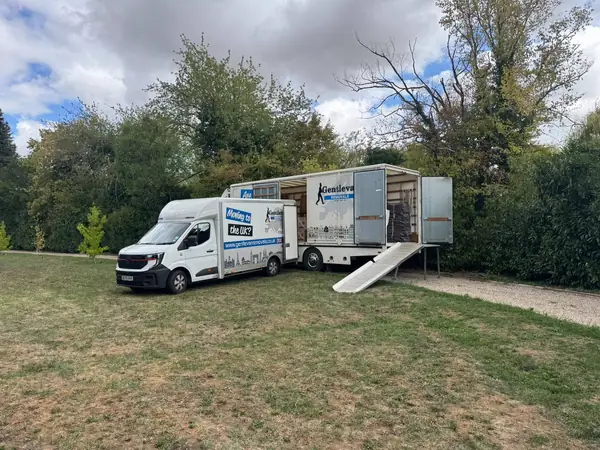 Gentlevan Removals box van parked on grass beside a Gentlevan lorry with its loading ramp down and side doors open, trees behind