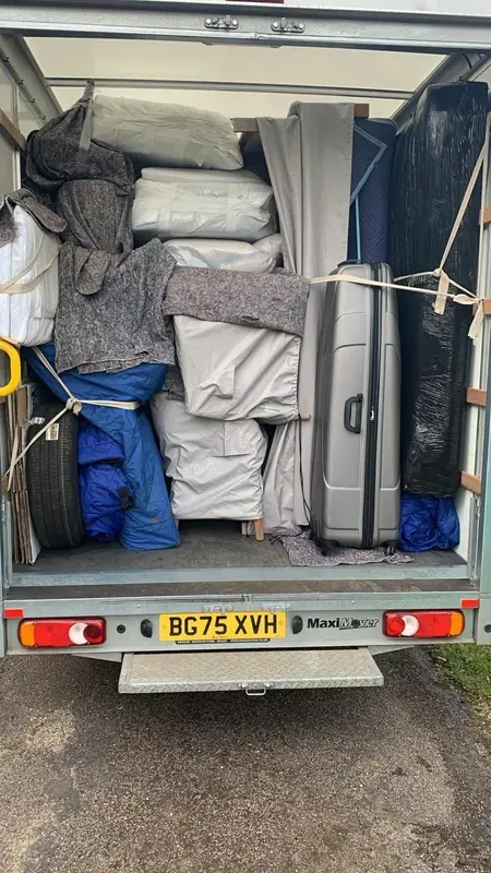 Rear of a loaded Gentlevan removal van with furniture wrapped in grey and blue blankets, a large suitcase and mattresses strapped in place