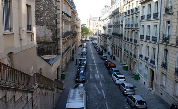Narrow European city street with cars parked tightly on both sides and a delivery vehicle loading