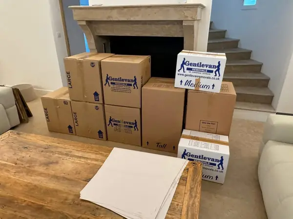 Gentlevan branded removal cartons in large, medium and tall sizes stacked ready for packing beside a stone fireplace, packing paper on the table