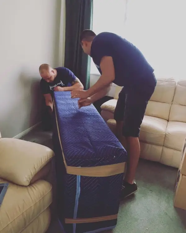 Two removal crew fitting a protective cover over a mattress in a living room