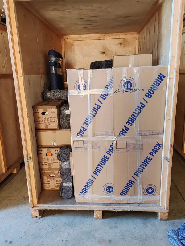 Inside a storage container: labelled boxes, blanket-wrapped furniture and mirror and picture packs stacked and secured