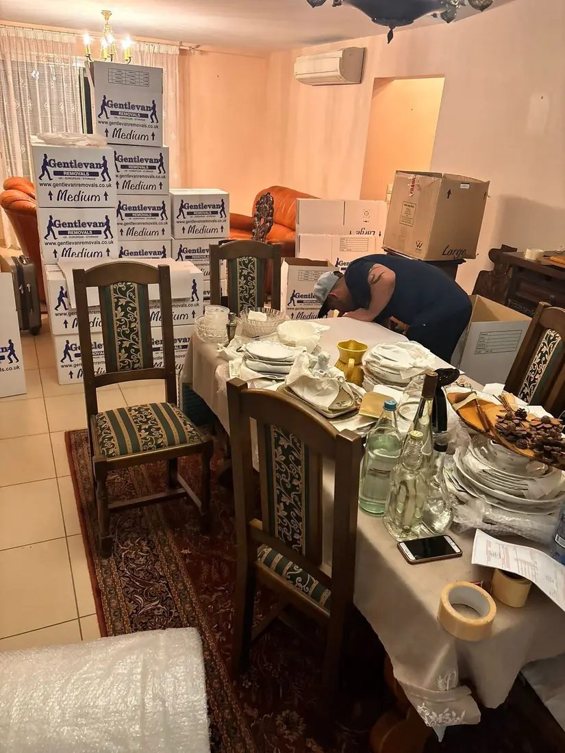 Gentlevan Removals crew member wrapping china and glassware at a dining table with branded cartons stacked behind