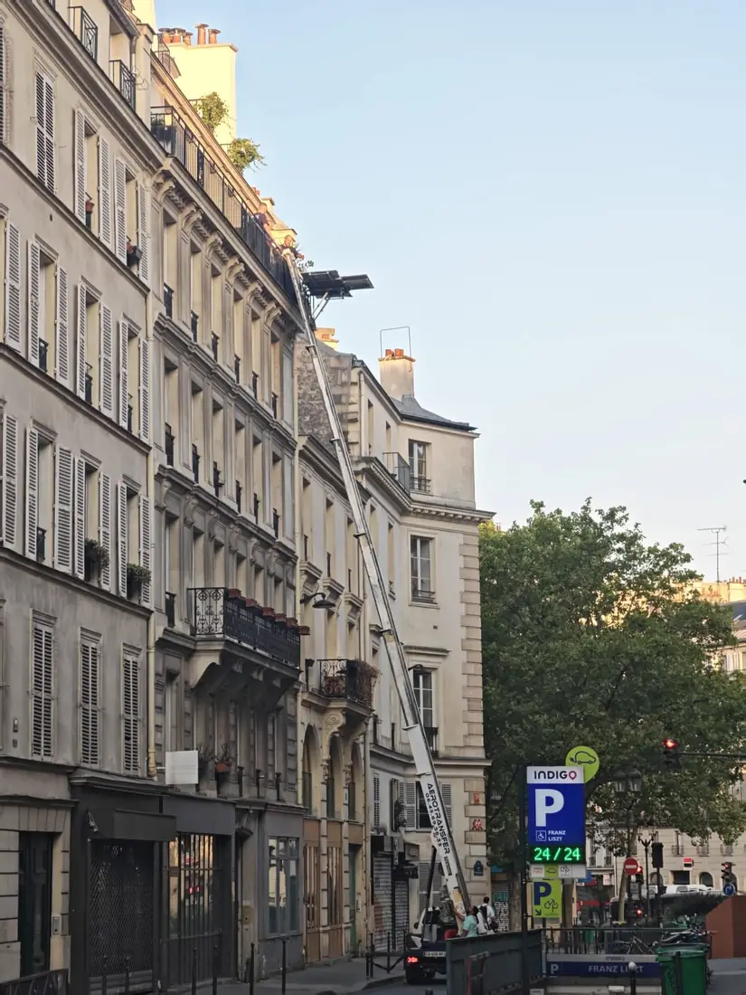 External furniture hoist raised to a top floor apartment window on a Paris street during a collection