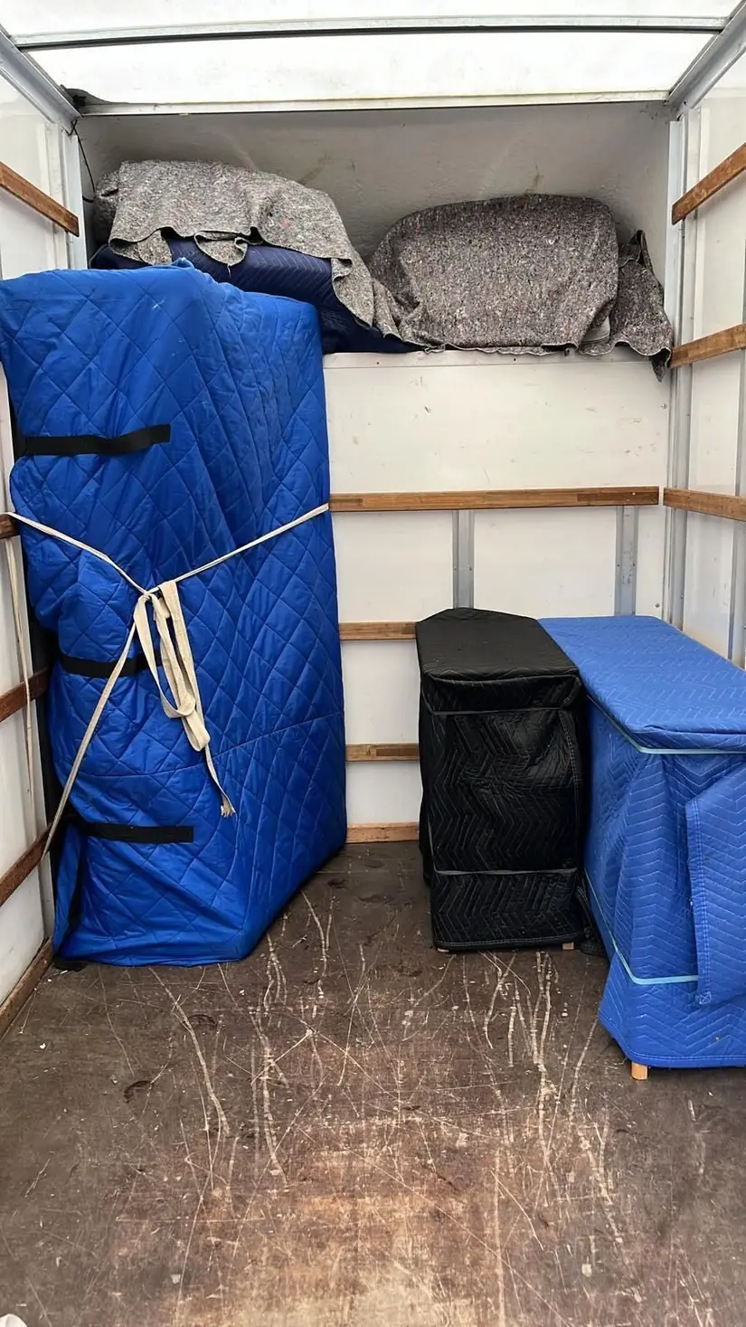 Inside a Gentlevan Removals vehicle, furniture in quilted covers strapped upright with felt blankets stowed overhead