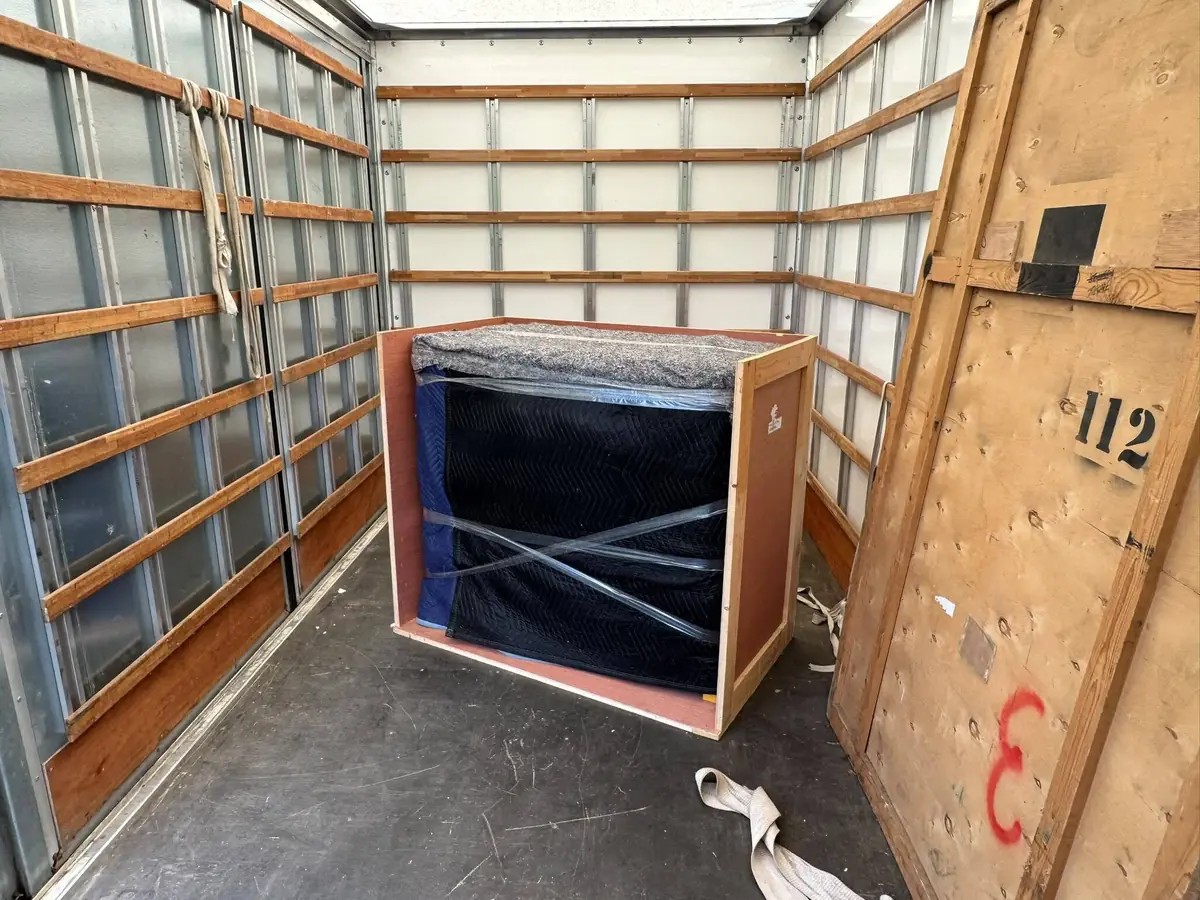 A blanket wrapped item secured inside a bespoke timber crate in the back of a Gentlevan vehicle, beside a large plywood transit case