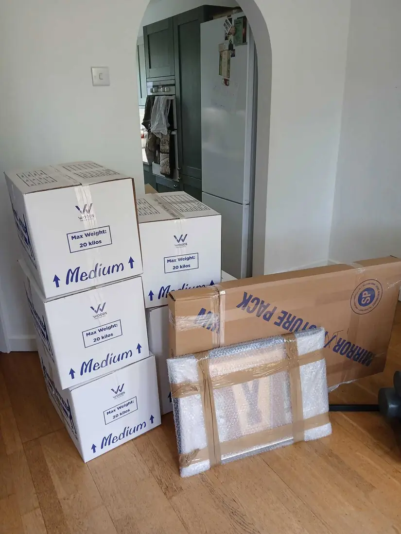 Taped Gentlevan medium cartons stacked beside a bubble wrapped picture and a flat mirror pack on a wooden floor