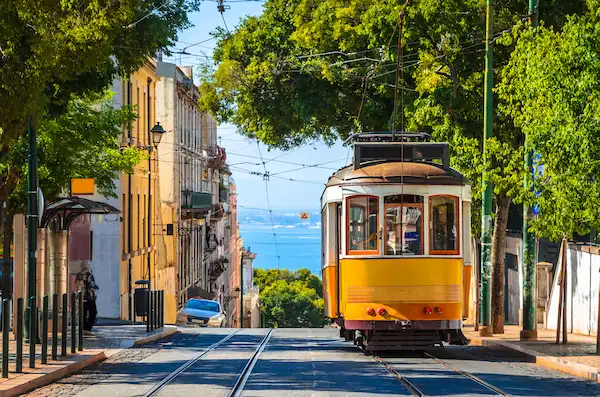 Yellow Lisbon tram on its tracks on a tree-lined street above the Tagus, Portugal