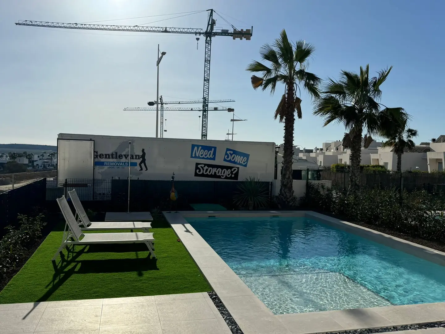 A Gentlevan Removals lorry standing beyond the pool of a newly built villa, with palm trees and tower cranes behind