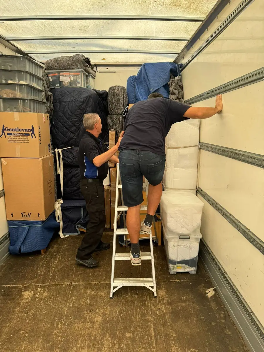 Two Gentlevan crew members loading and stacking a customer's belongings inside the vehicle, one working from a stepladder