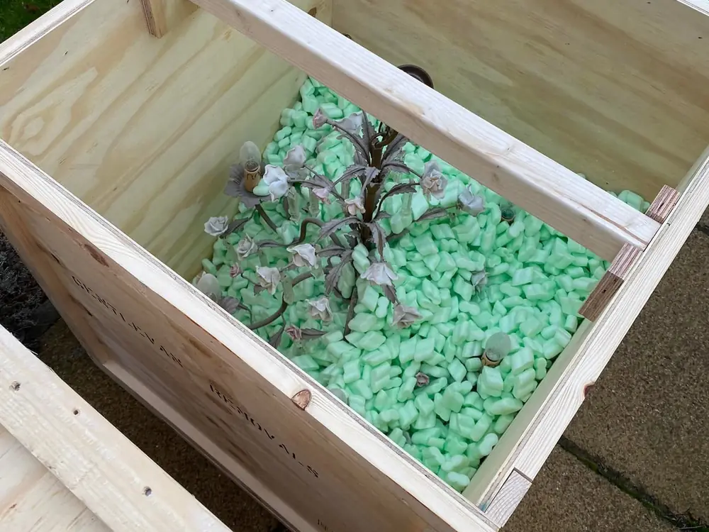 A Gentlevan Removals plywood crate part filled with loose fill chips, protecting a delicate metal and porcelain chandelier