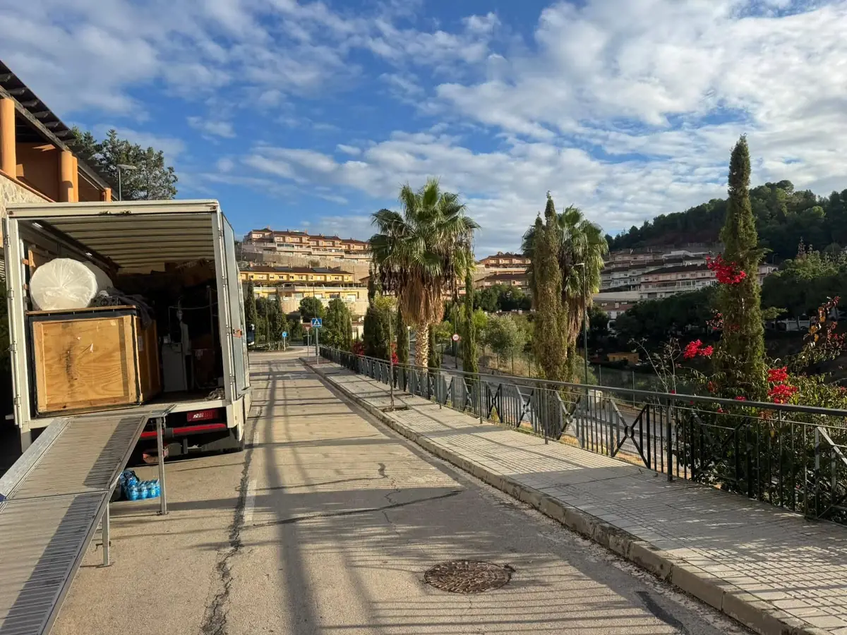Gentlevan Removals vehicle with the loading ramp down on a hillside street of terracotta-roofed apartments and palms