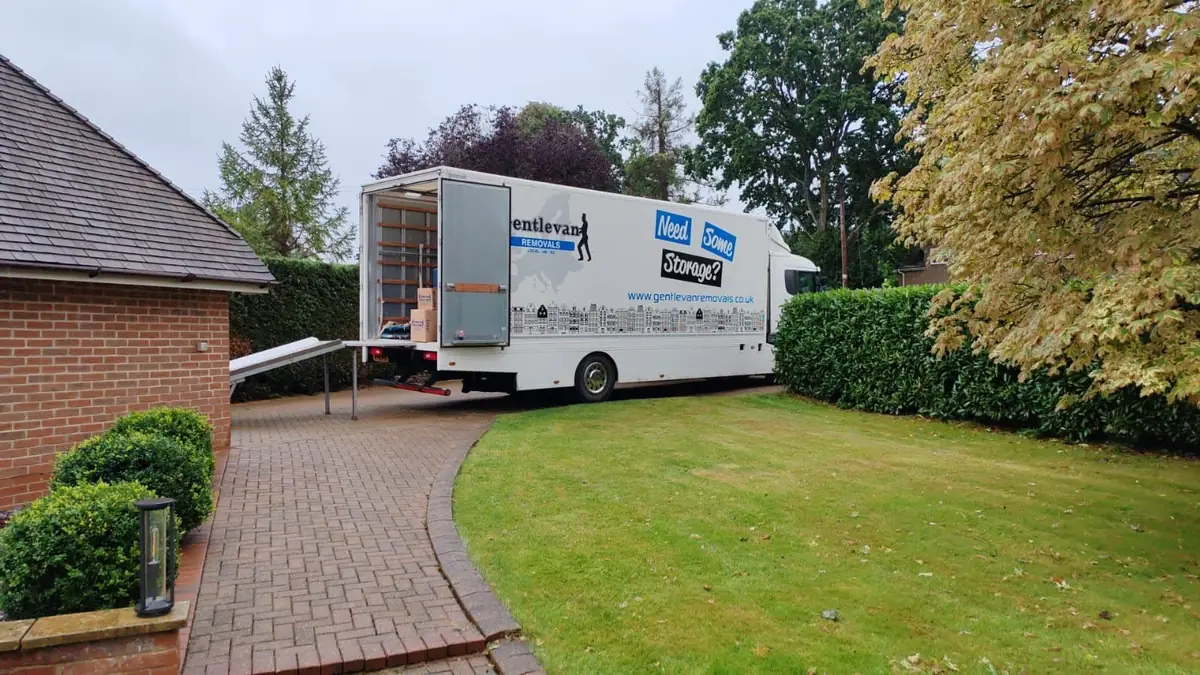 Gentlevan Removals lorry with the tail lift and ramp down on a block paved driveway beside a brick house, cartons visible inside the vehicle