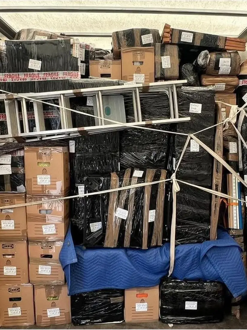 Inside a loaded Gentlevan Removals vehicle with labelled cartons, shrink wrapped furniture and blankets strapped in place against the side rails