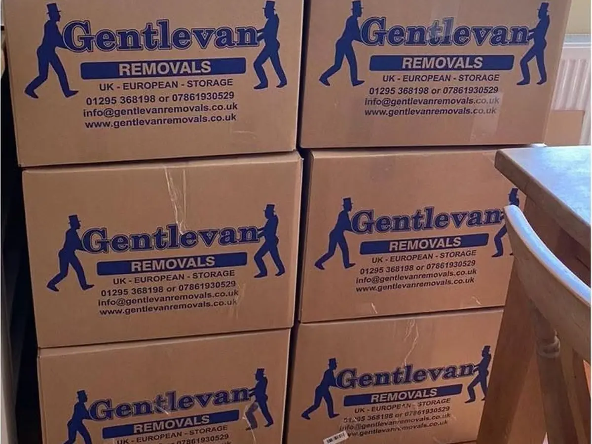Gentlevan Removals branded cartons stacked and labelled ready for loading beside a wooden staircase