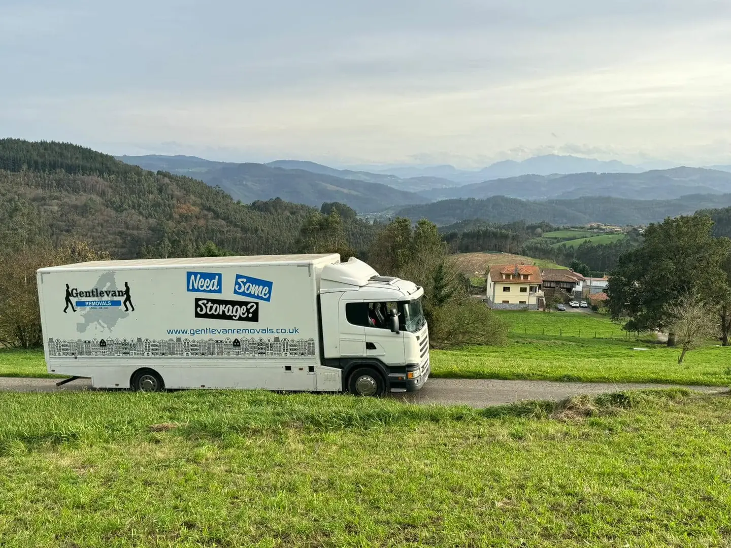 A Gentlevan Removals lorry and trailer on the road through northern Spain, with wooded valleys and mountains beyond